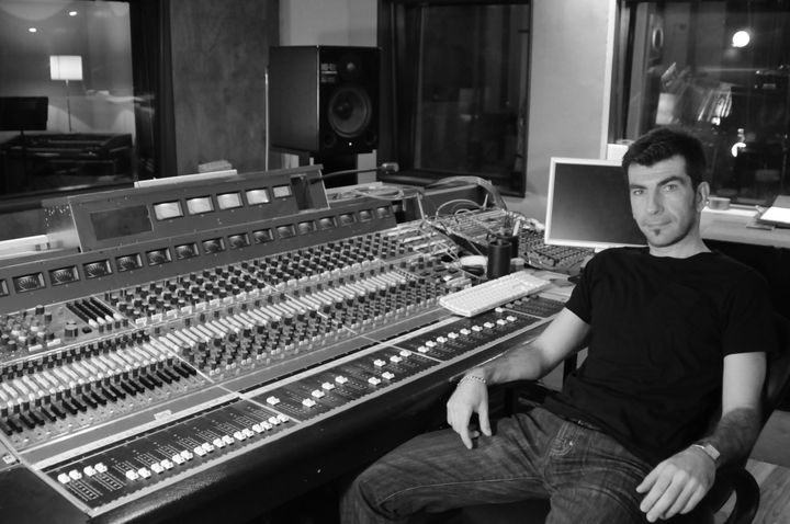 Haig V. seated beside a large mixing console in a studio, looking into the camera.