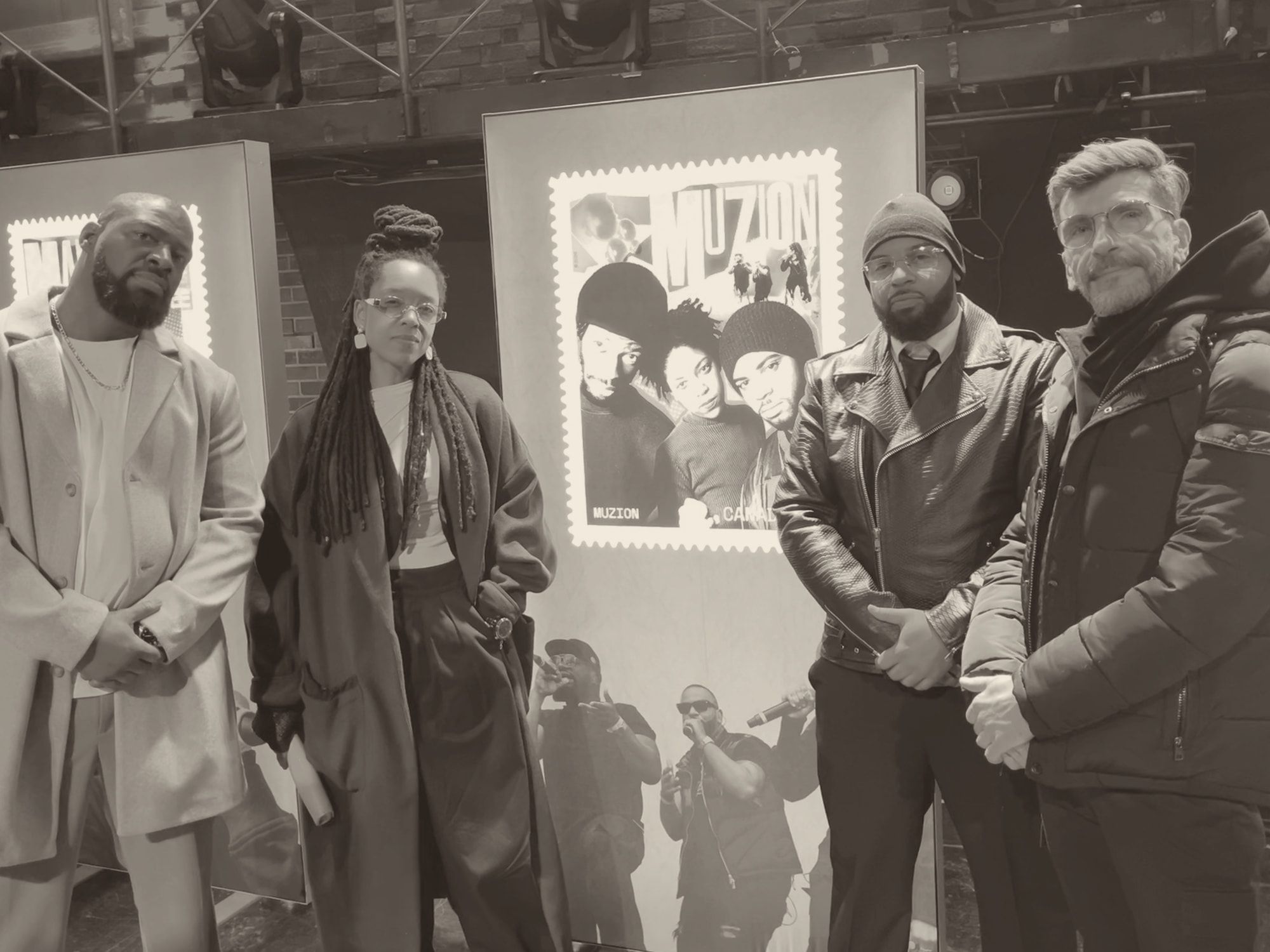 Haig V. with the three members of Muzion in front of a lit display of their Canada Post stamp.
